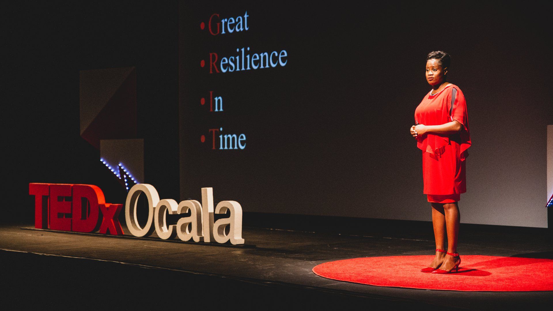 A woman in a red dress is standing on a stage in front of a ted ocala sign.