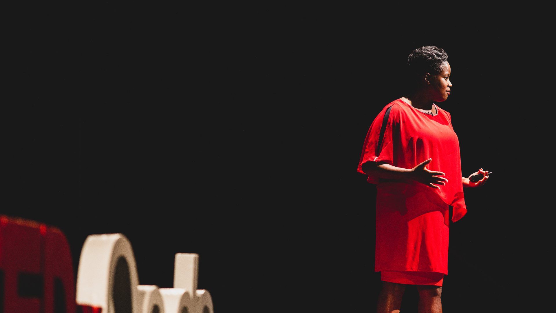 A woman in a red dress is standing on a stage giving a speech.