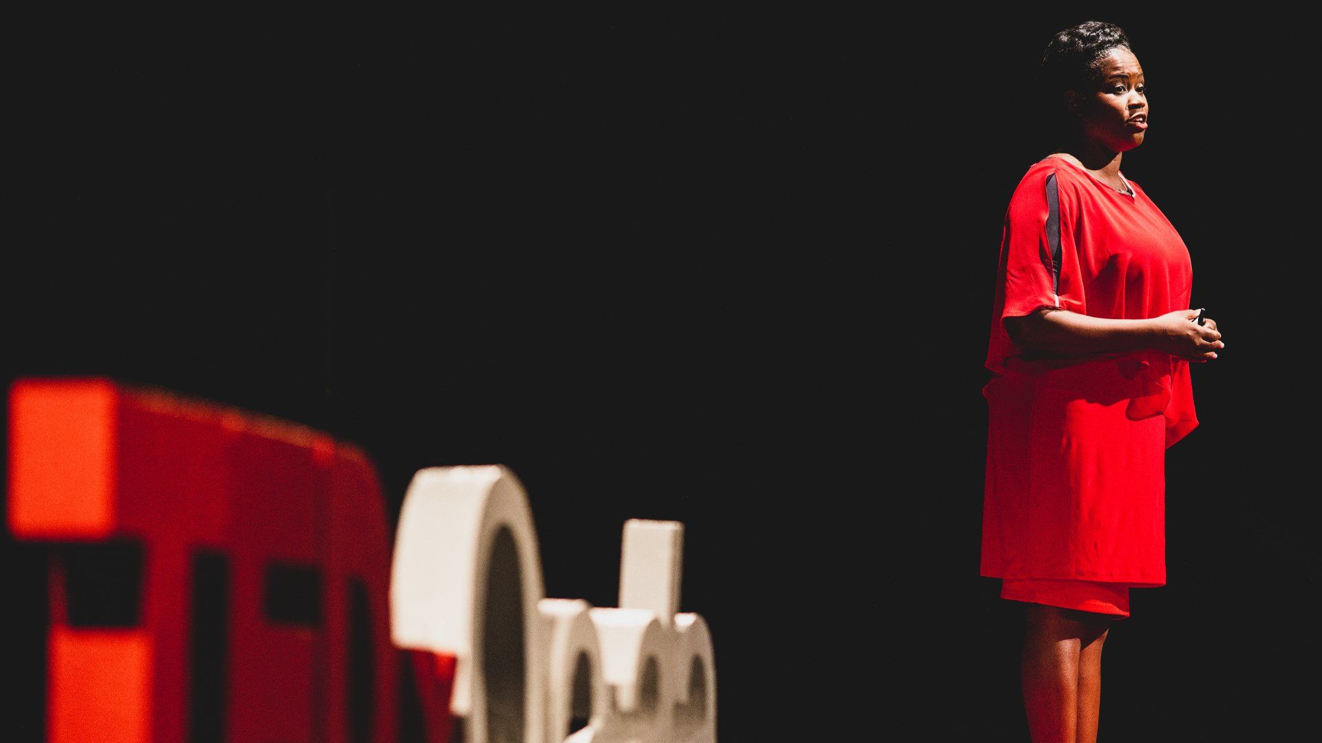 A woman in a red dress is standing in front of a ted talk sign.