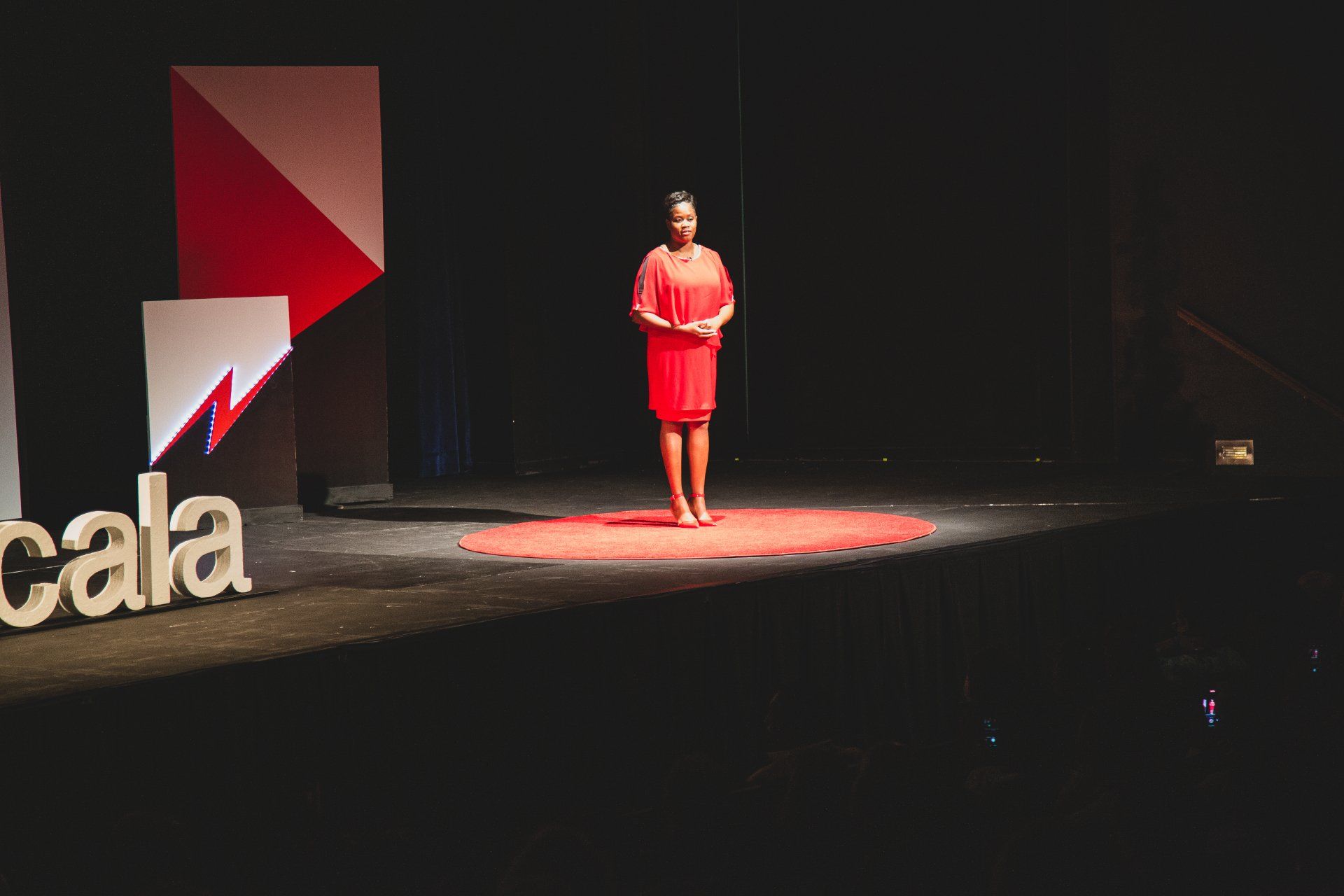A woman in a red dress is standing on a stage in front of a sign that says cala.