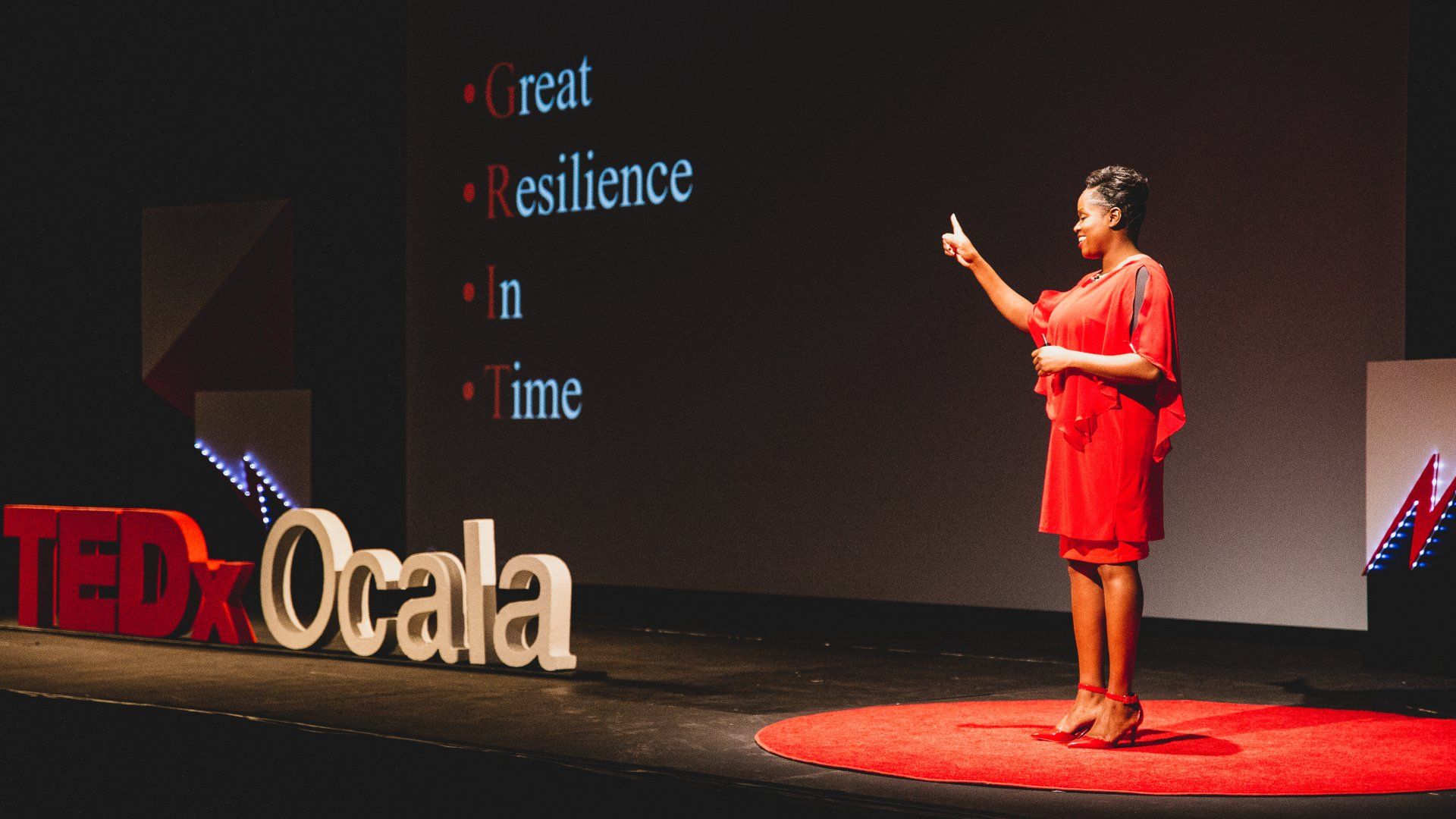 A woman in a red dress is giving a speech at tedx ocala