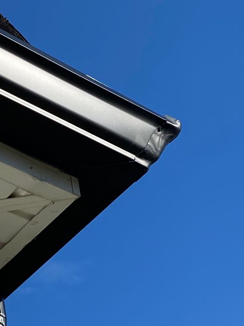 Black guttering on the corner of a building, against a bright blue sky.