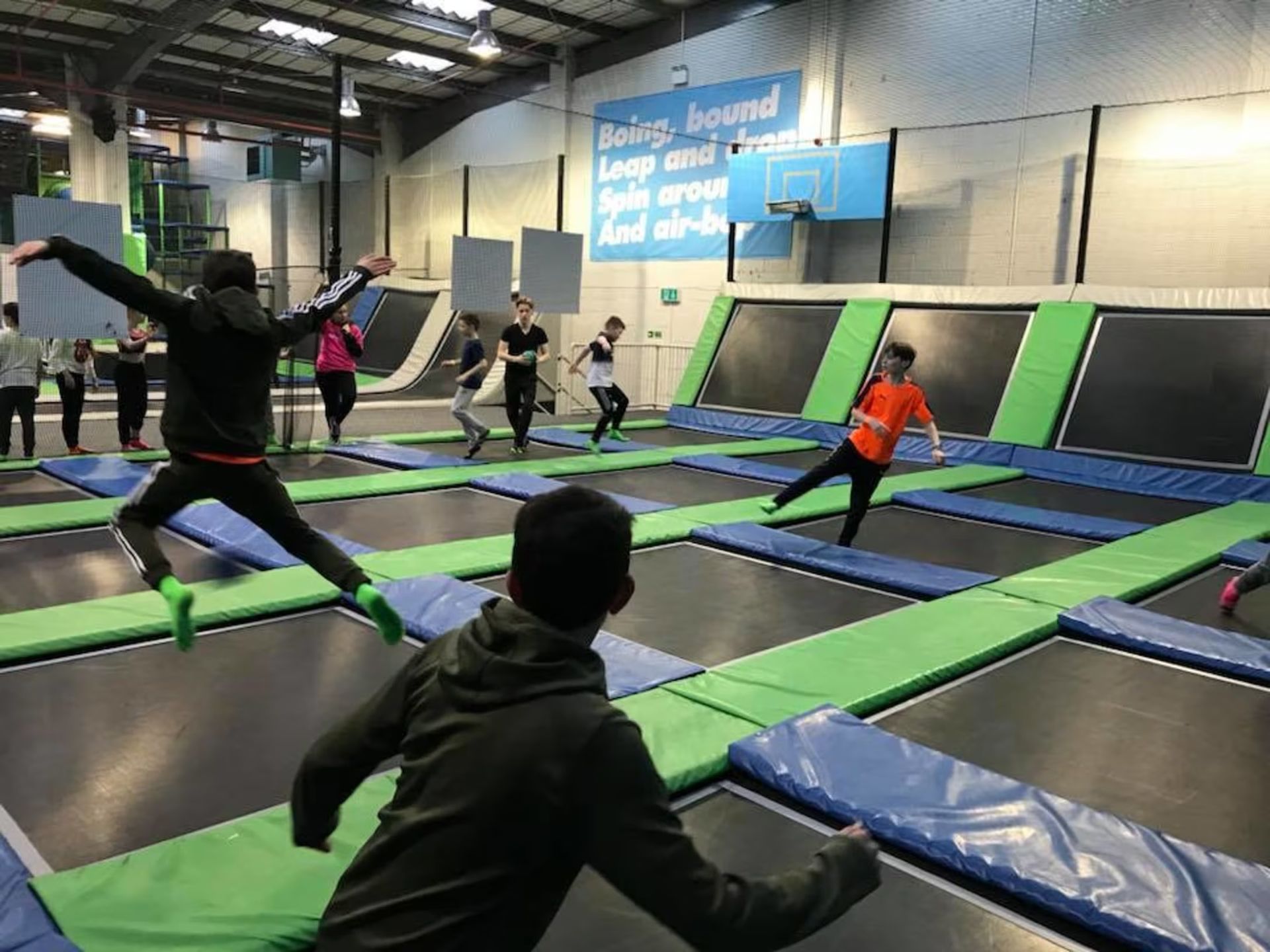 People jumping and running on indoor trampolines with green and blue pads.