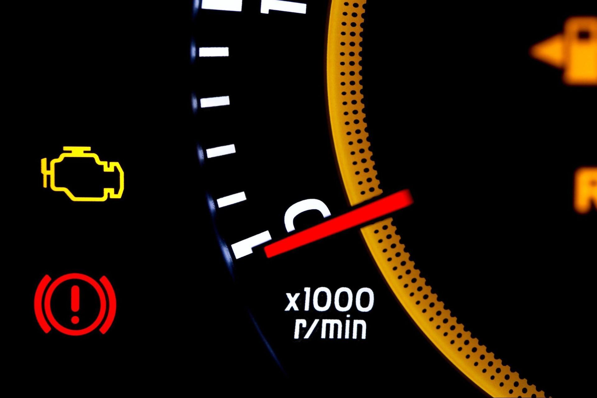 Close-up of a vehicle dashboard showing a yellow check engine light and a red brake warning light.