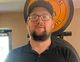 A man with a beard and glasses is standing in front of a tire.