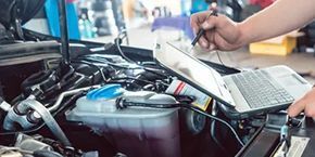 A person is working on a car with a laptop and a tablet performing diagnostics.
