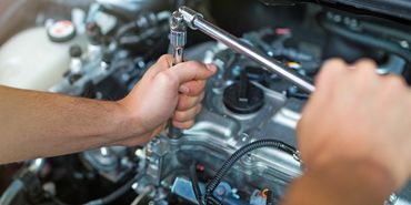 A man is working on a car engine with a wrench.