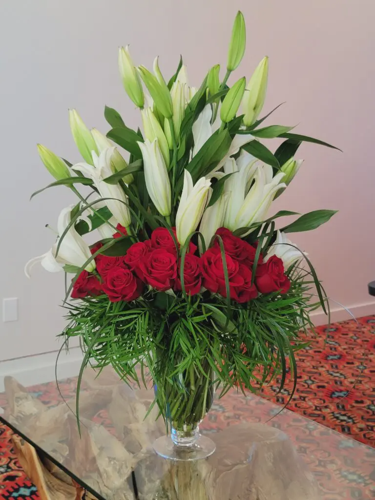 A vase filled with white lilies and red roses on a glass table.
