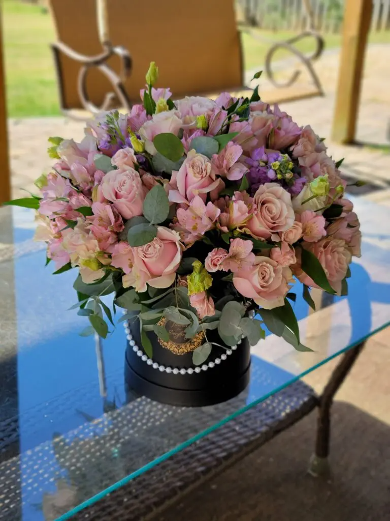 A black box filled with pink flowers is sitting on a glass table.