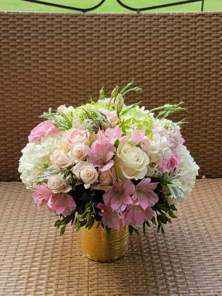 A vase filled with pink and white flowers is sitting on a wicker table.