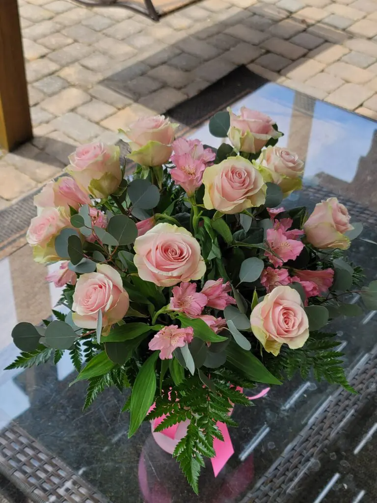 A vase filled with pink roses and greenery is sitting on a table.