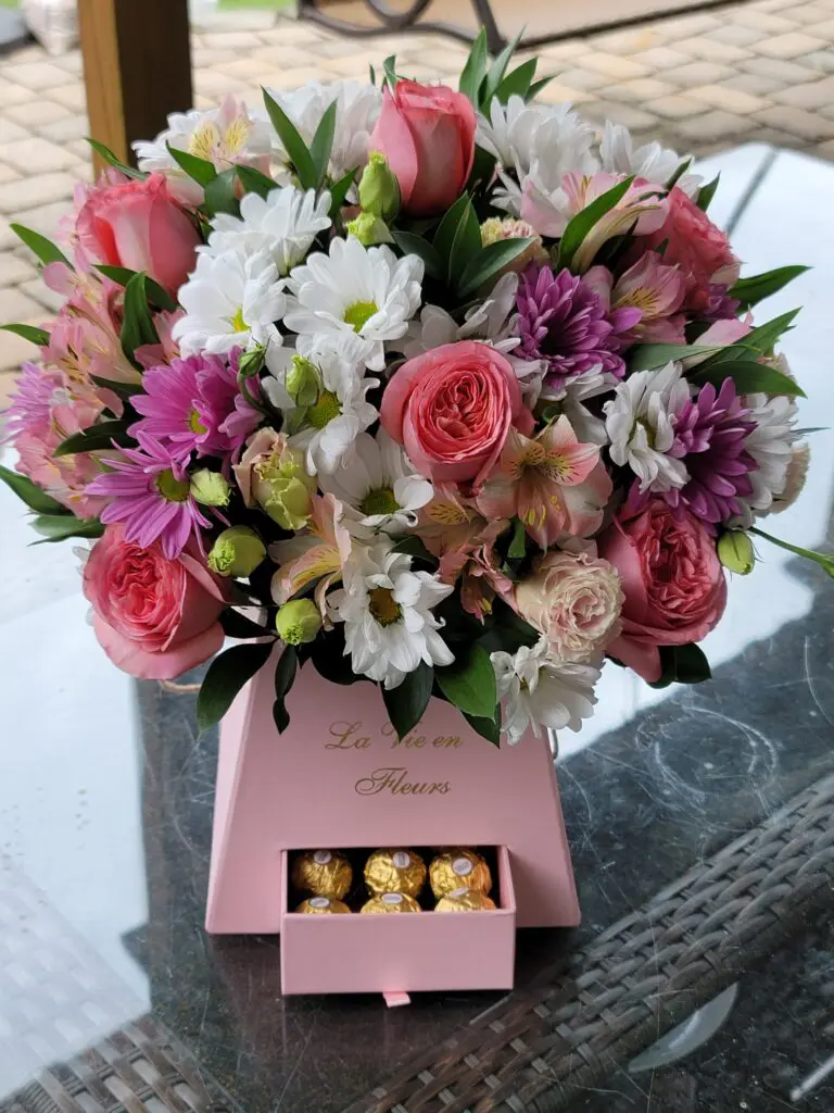 A pink box filled with flowers and chocolates on a table.