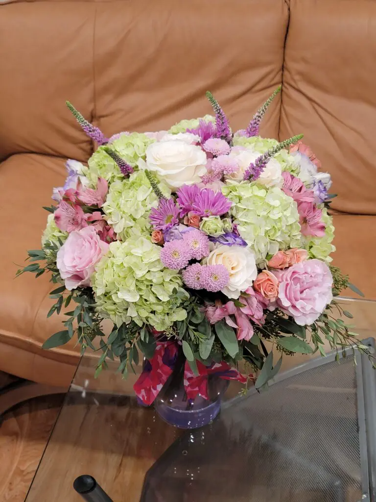 A vase filled with flowers is sitting on a glass table next to a couch.