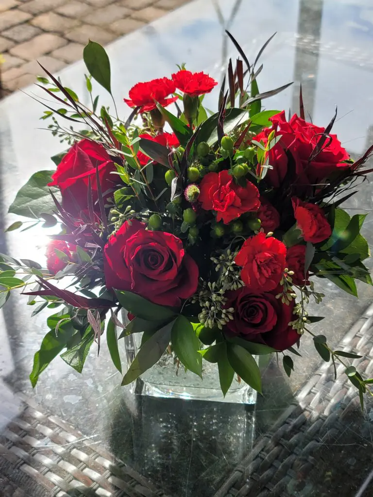 A vase filled with red roses and carnations is sitting on a table.