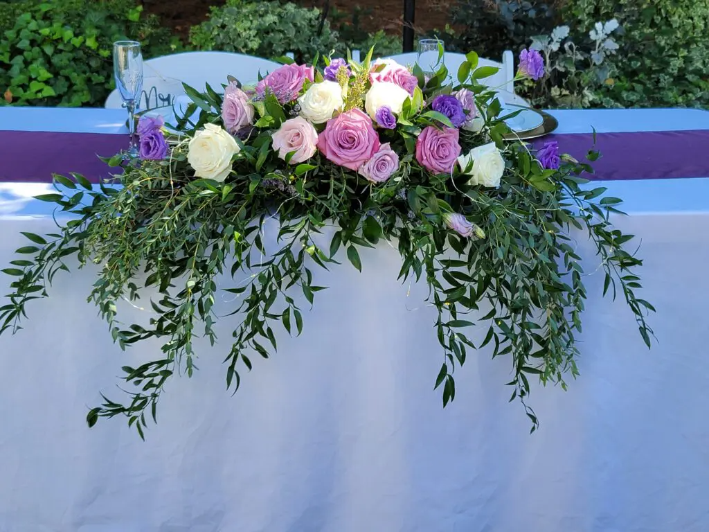 A table with purple and white flowers and greenery on it.