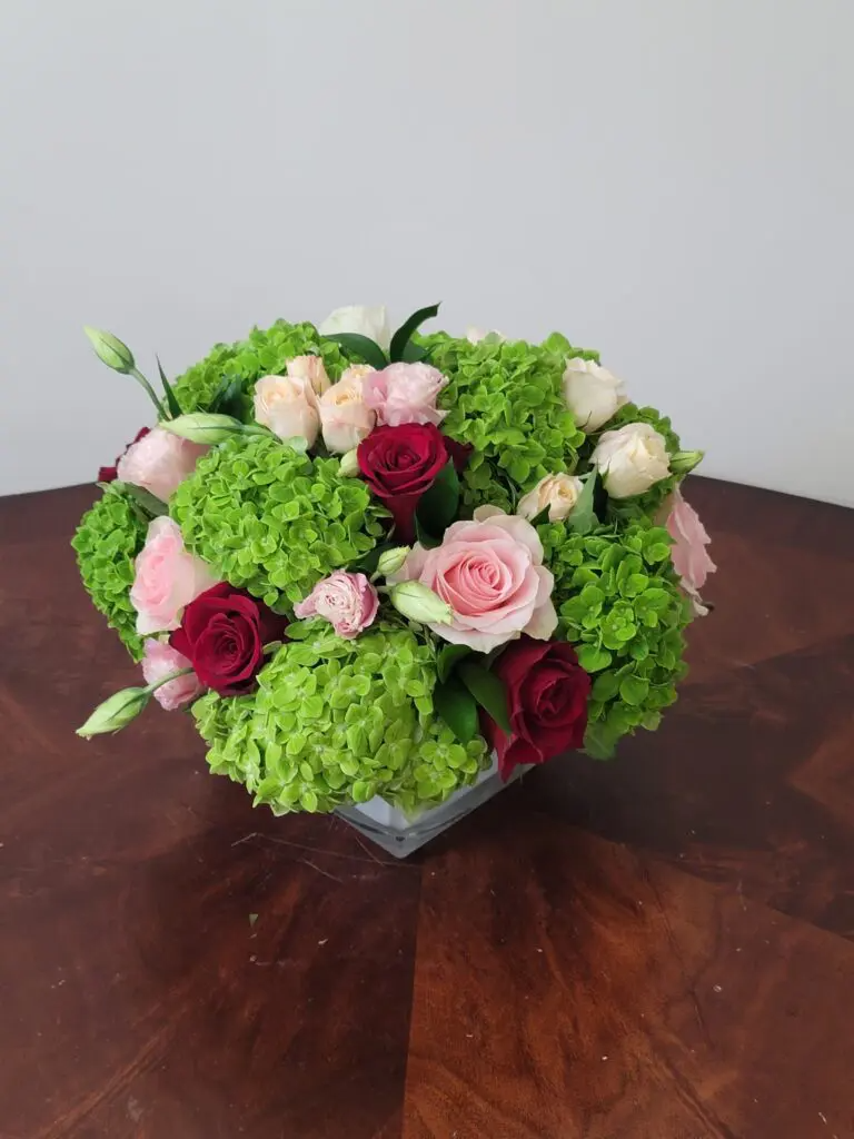 A vase filled with pink and red flowers is sitting on a wooden table.
