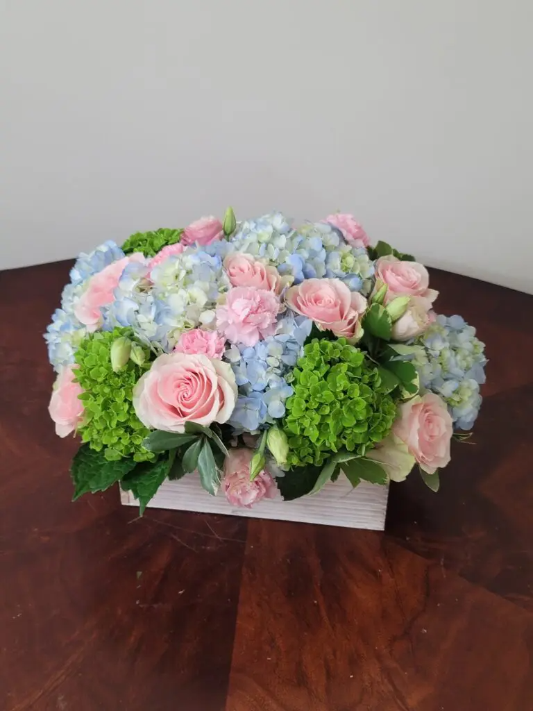 A wooden box filled with pink and blue flowers is sitting on a wooden table.