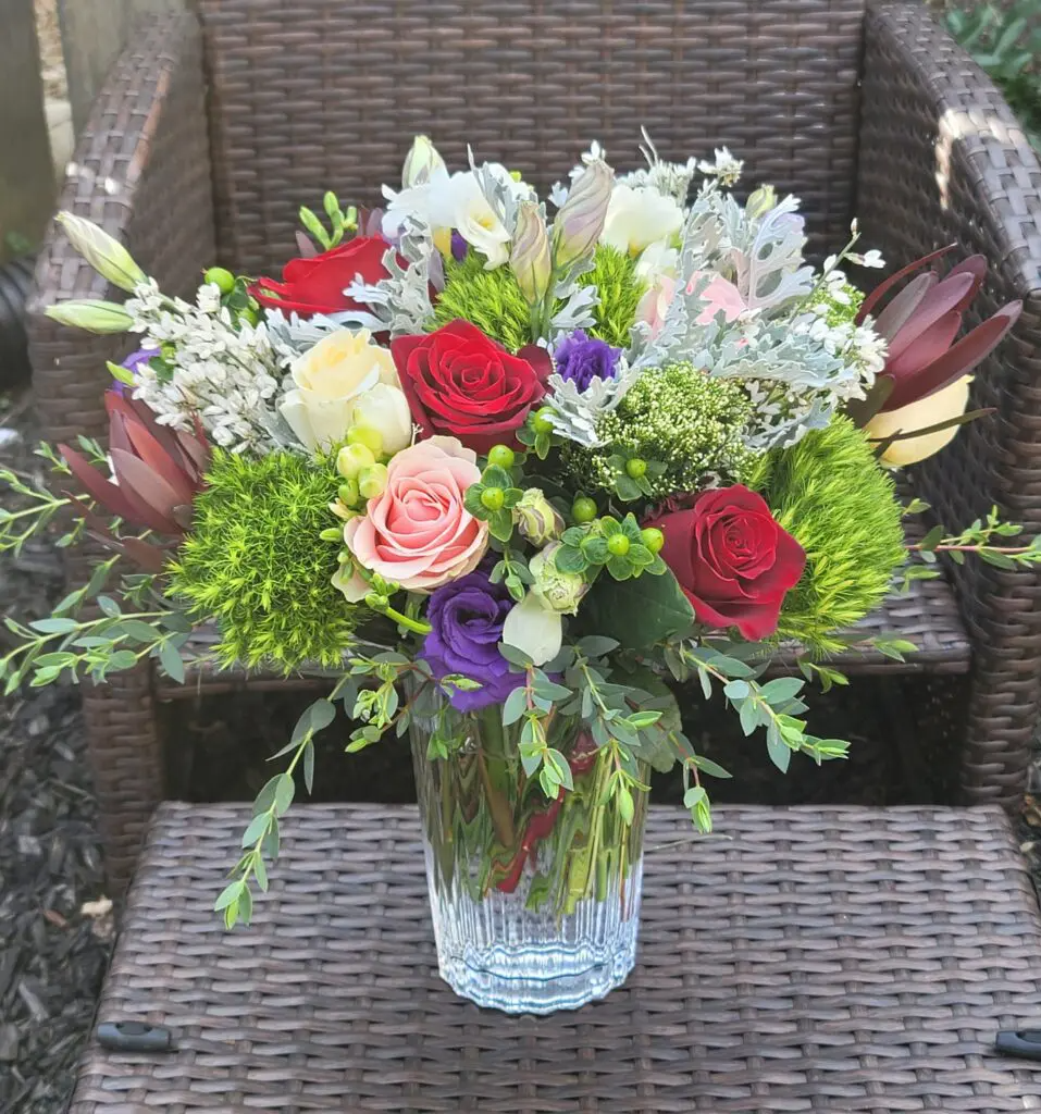 A vase filled with flowers is sitting on a table next to a chair.