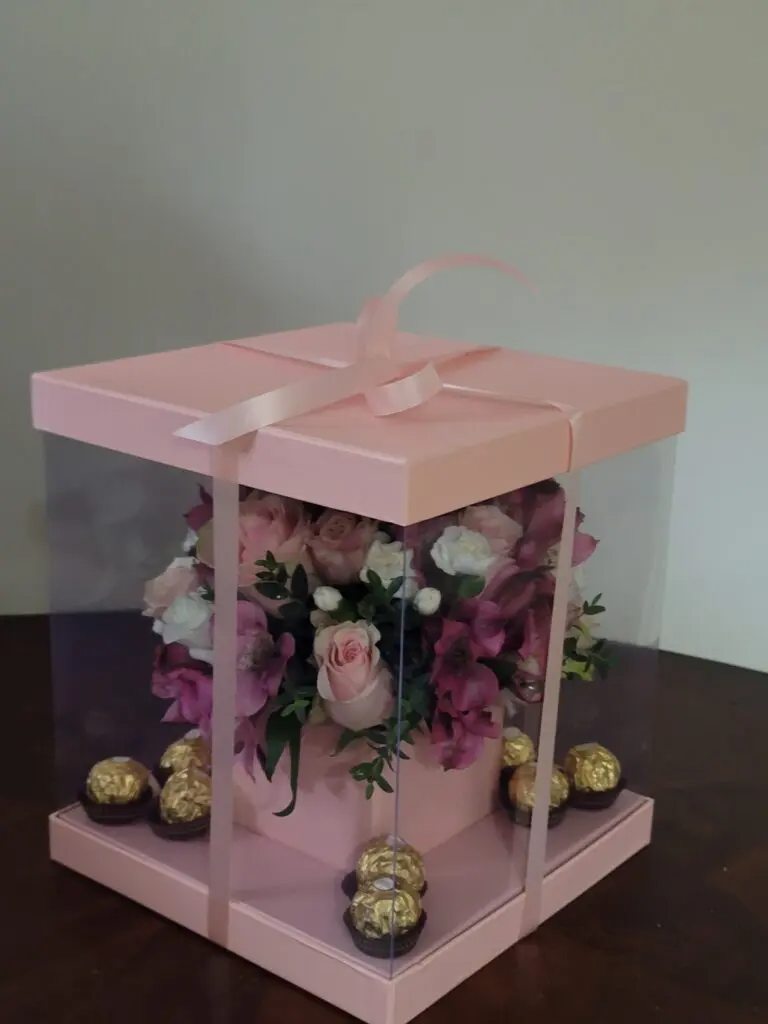 A pink box filled with flowers and chocolates on a table