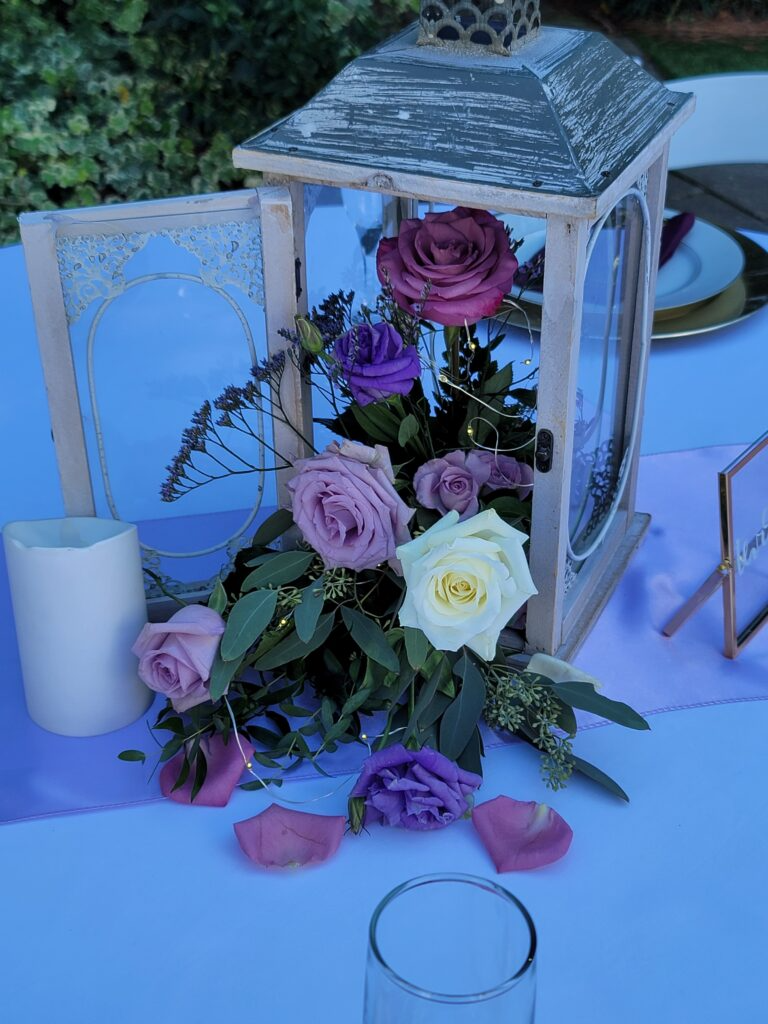 A lantern filled with purple and white roses is on a table.