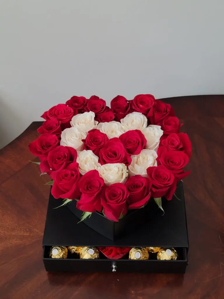 A heart shaped box filled with red and white roses and chocolates