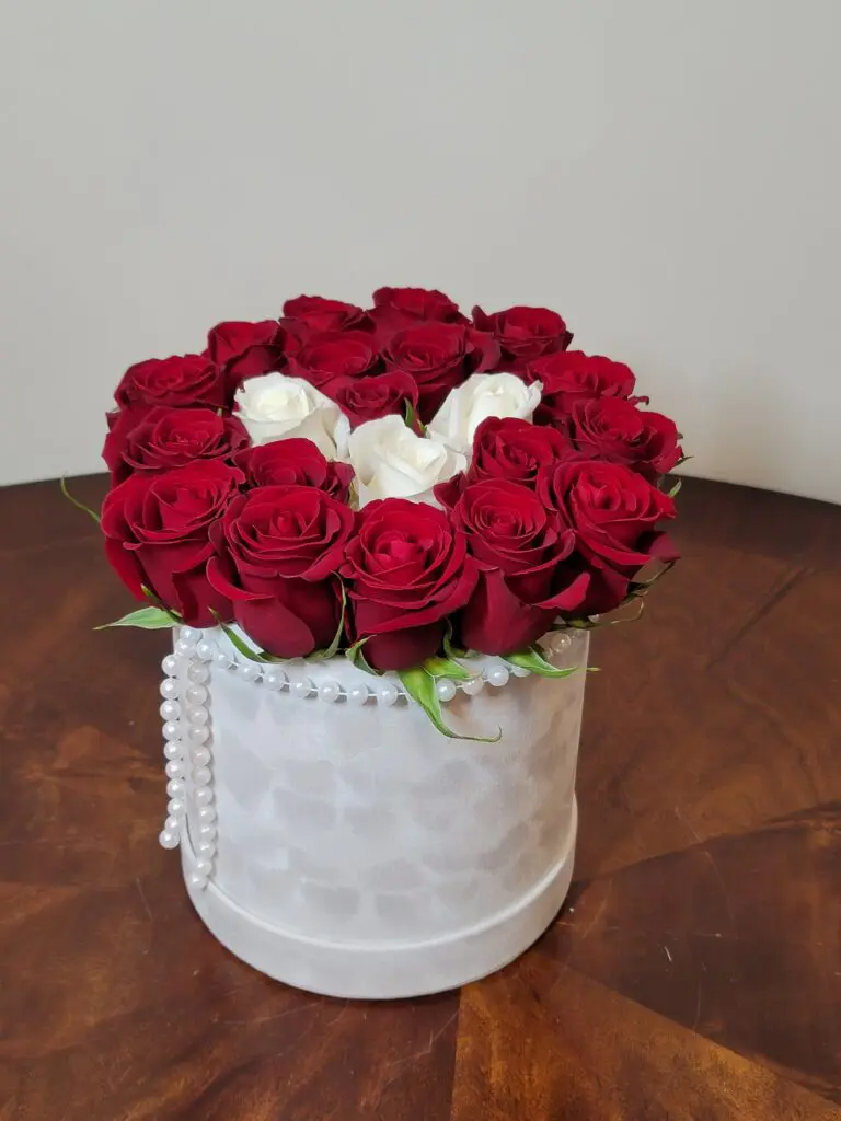 A white box filled with red and white roses and pearls.