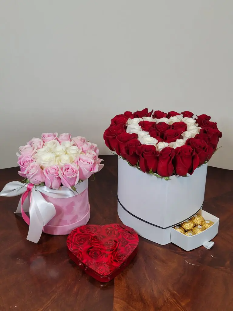 Two boxes of roses and a heart shaped box of chocolates on a table.