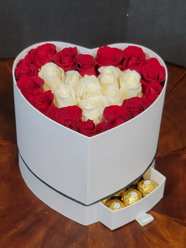 A heart shaped box filled with red and white roses and chocolates.