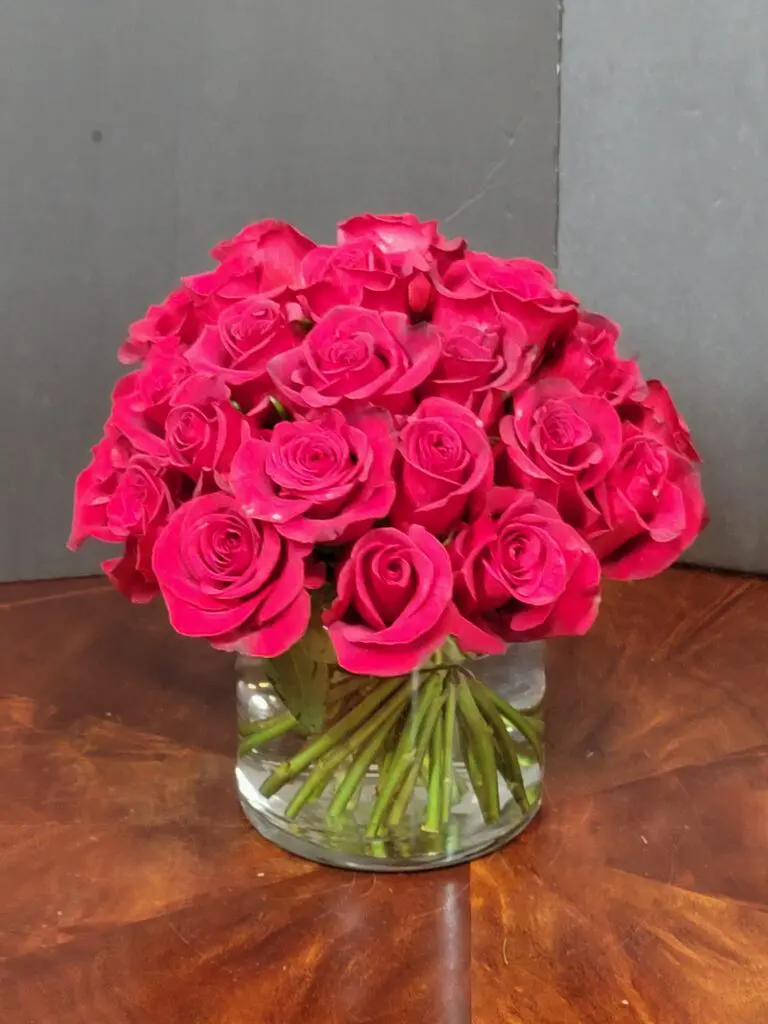 A vase filled with red roses is sitting on a wooden table.