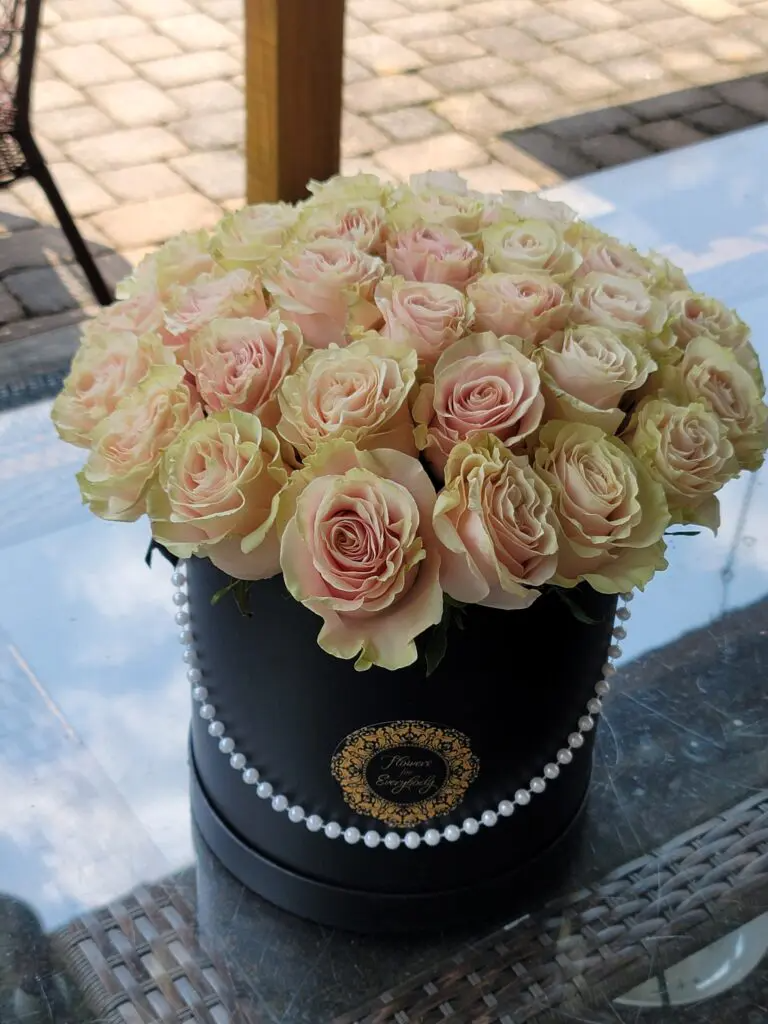 A black box filled with pink roses and pearls on a table.
