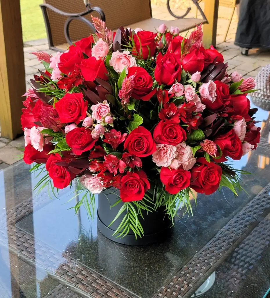A vase filled with red roses and pink carnations is sitting on a glass table.