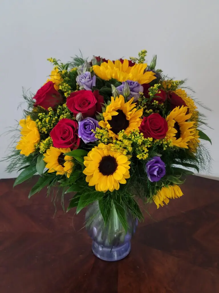 A vase filled with sunflowers and roses on a table.