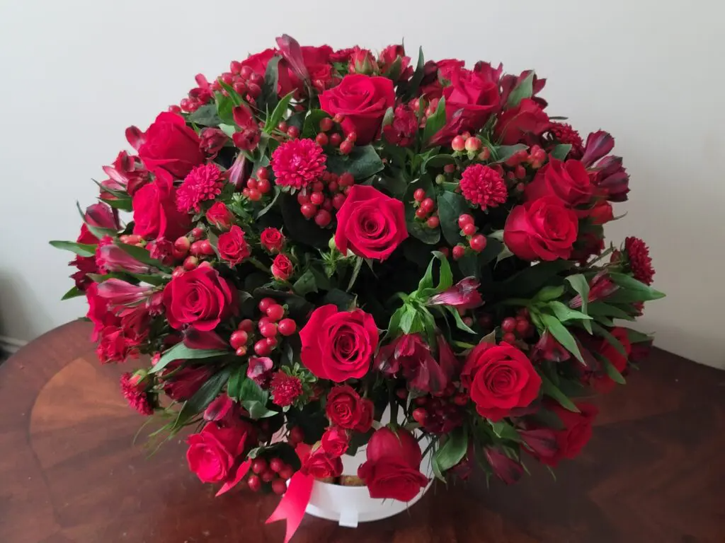 A vase filled with red roses and carnations is sitting on a wooden table.