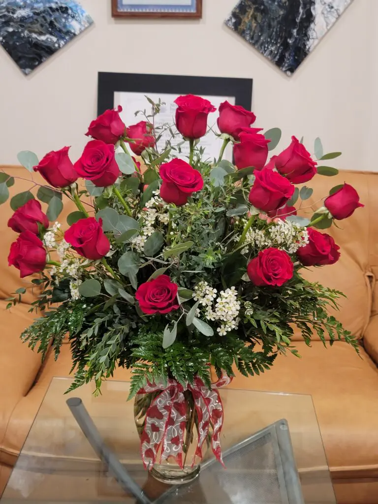 A vase filled with red roses is sitting on a glass table.