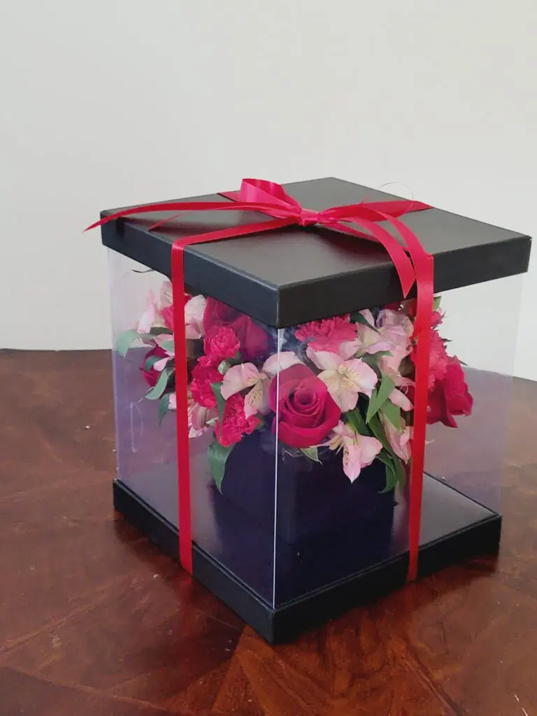 A clear box filled with flowers is sitting on a wooden table.