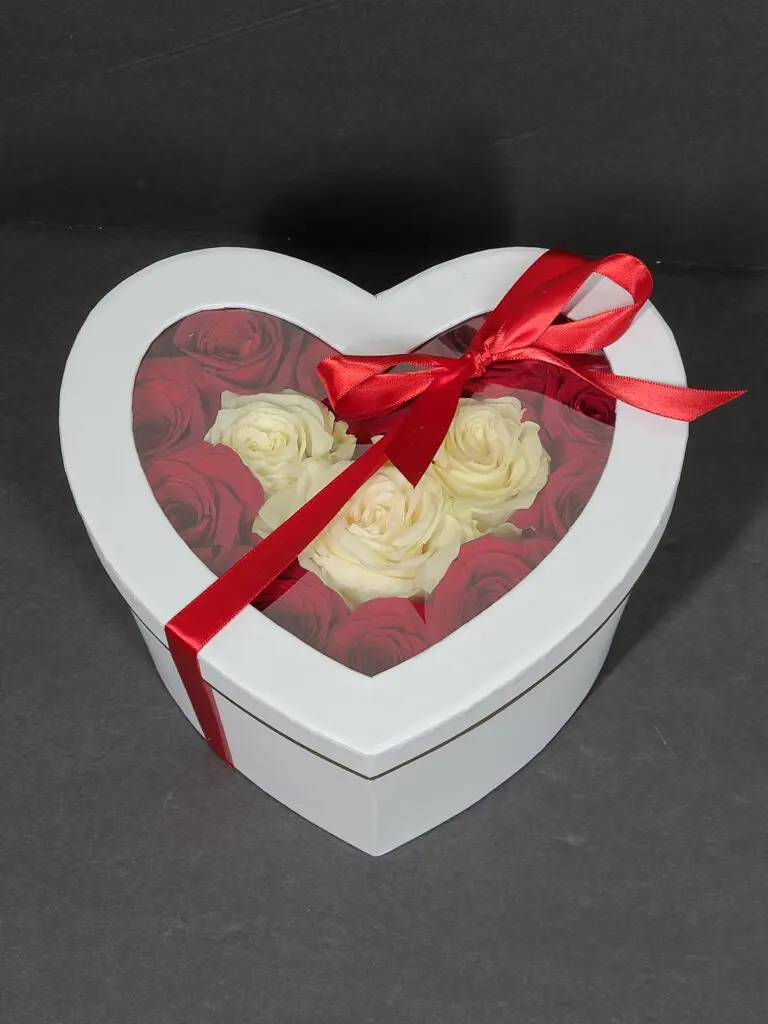 A heart shaped box filled with red and white roses with a red ribbon.