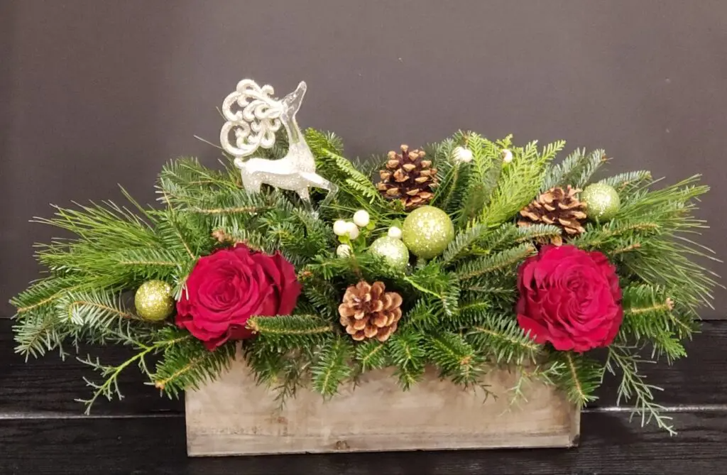 A wooden box filled with red roses , pine cones , and christmas decorations.