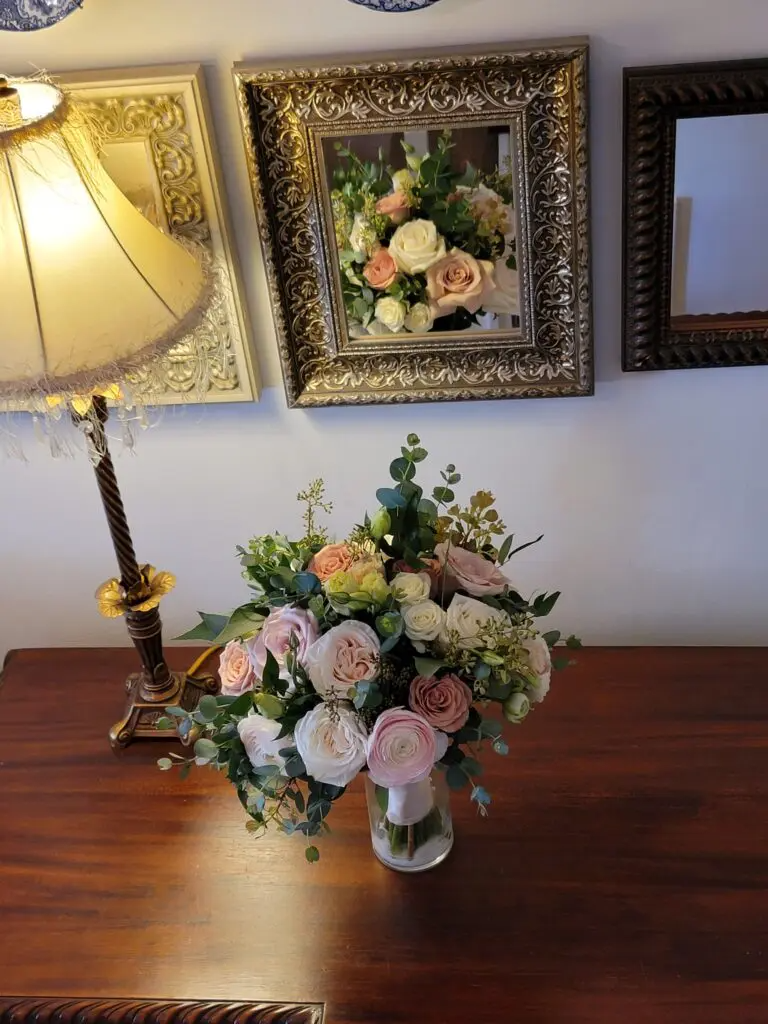 A vase of flowers is sitting on a wooden table next to a lamp.