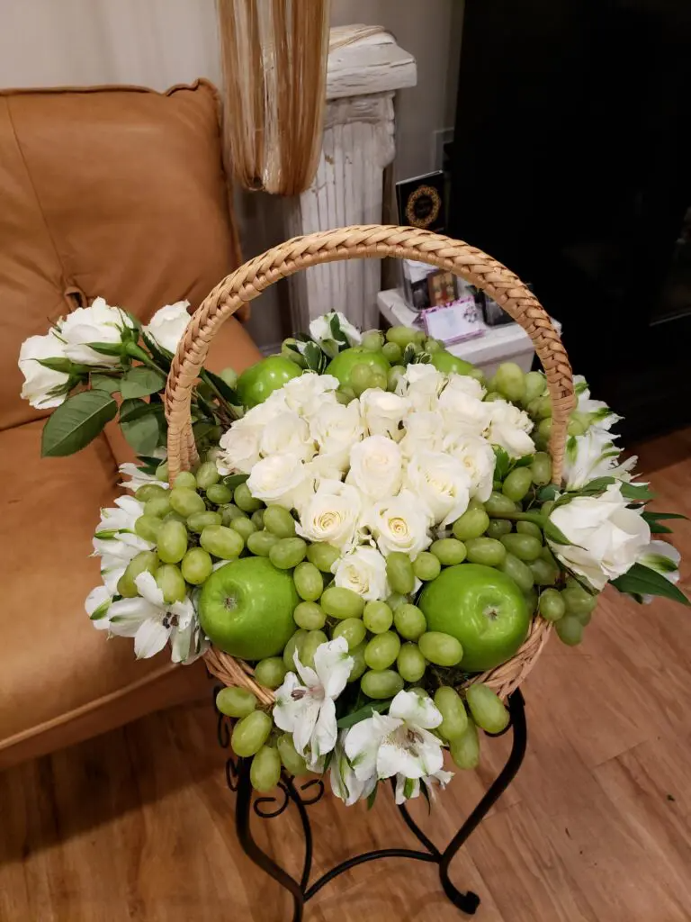 A basket filled with green grapes , white roses and apples.