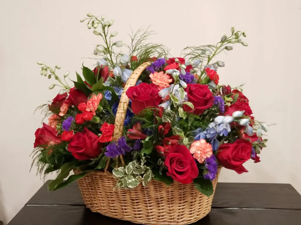 A wicker basket filled with red roses and blue carnations