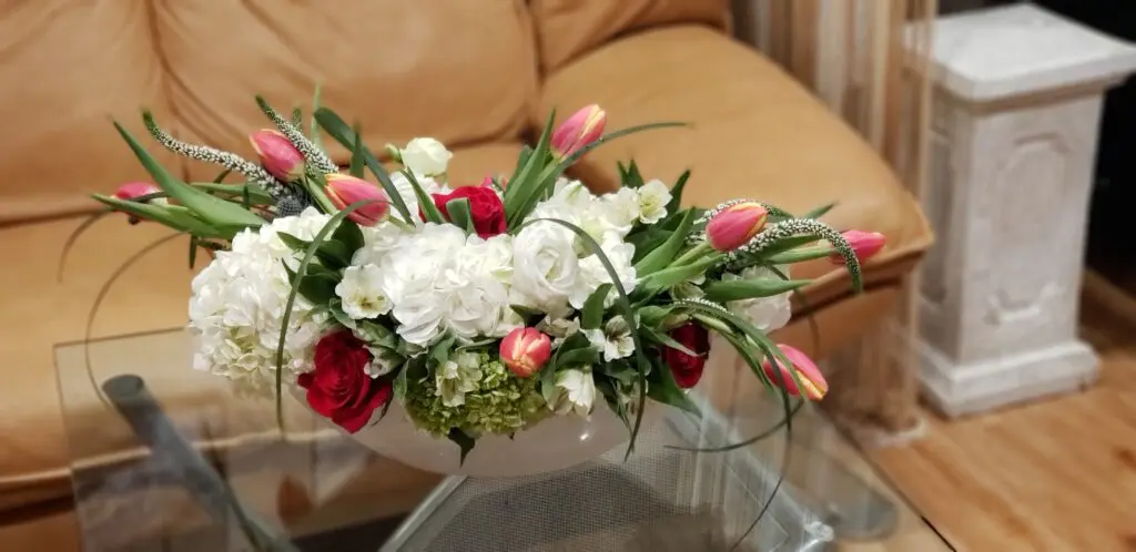 A vase of flowers is sitting on a glass table next to a couch.