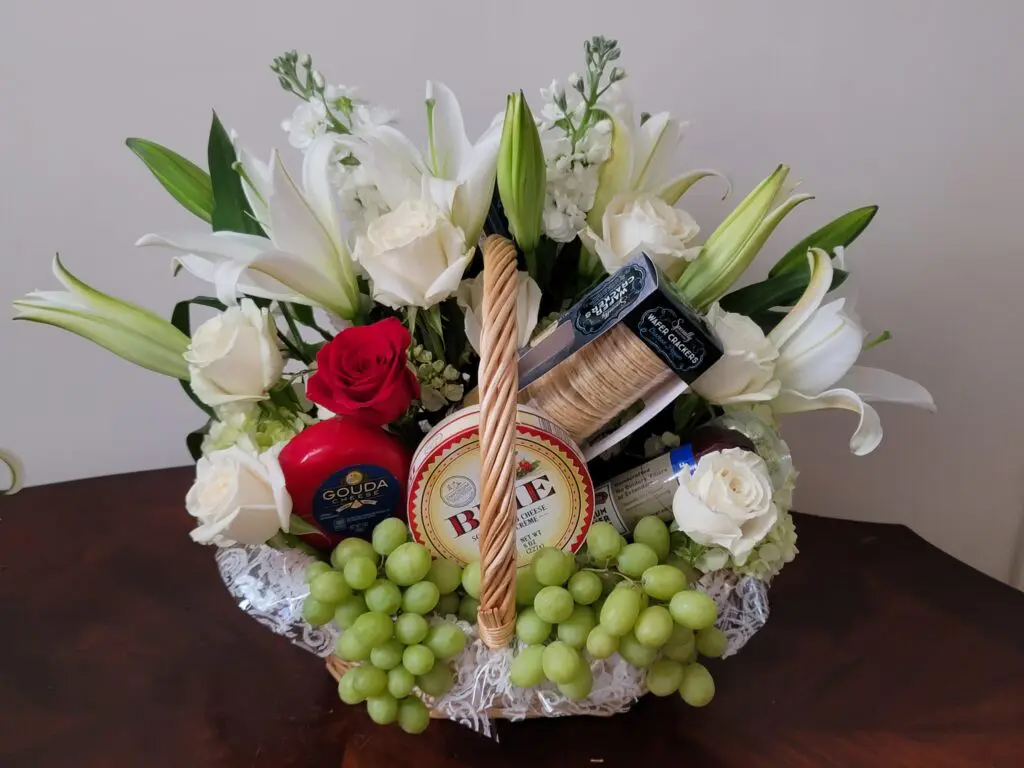 A basket filled with grapes , cheese , crackers and flowers on a table.