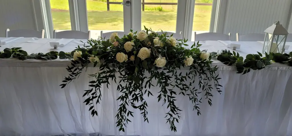 A long white table with flowers and greenery on it.