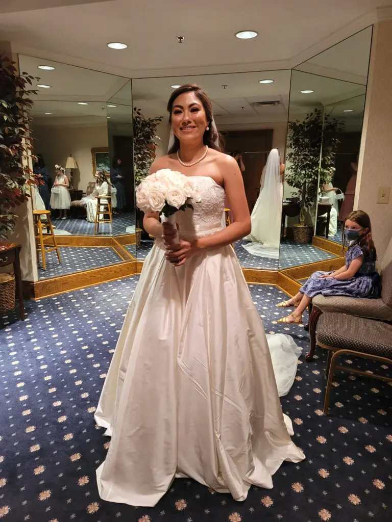 A woman in a wedding dress is standing in front of a mirror holding a bouquet of flowers.