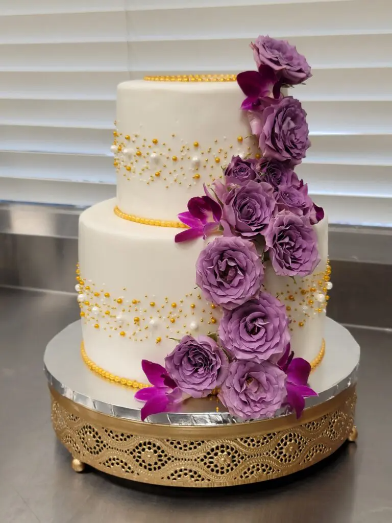 A white wedding cake with purple roses and pearls