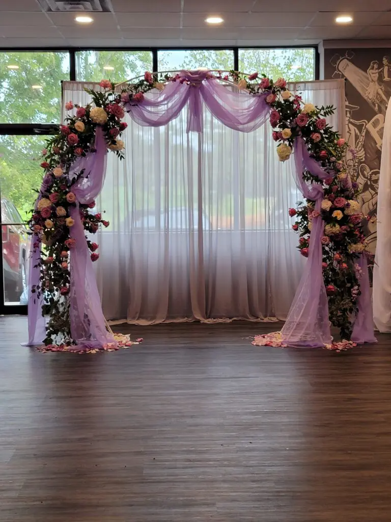 A room with a purple arch decorated with flowers and curtains.