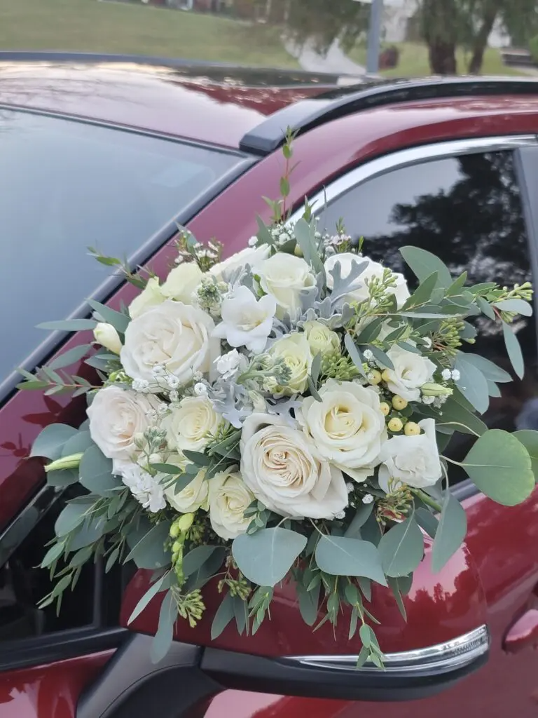 A red car with a bouquet of white flowers on the side mirror.