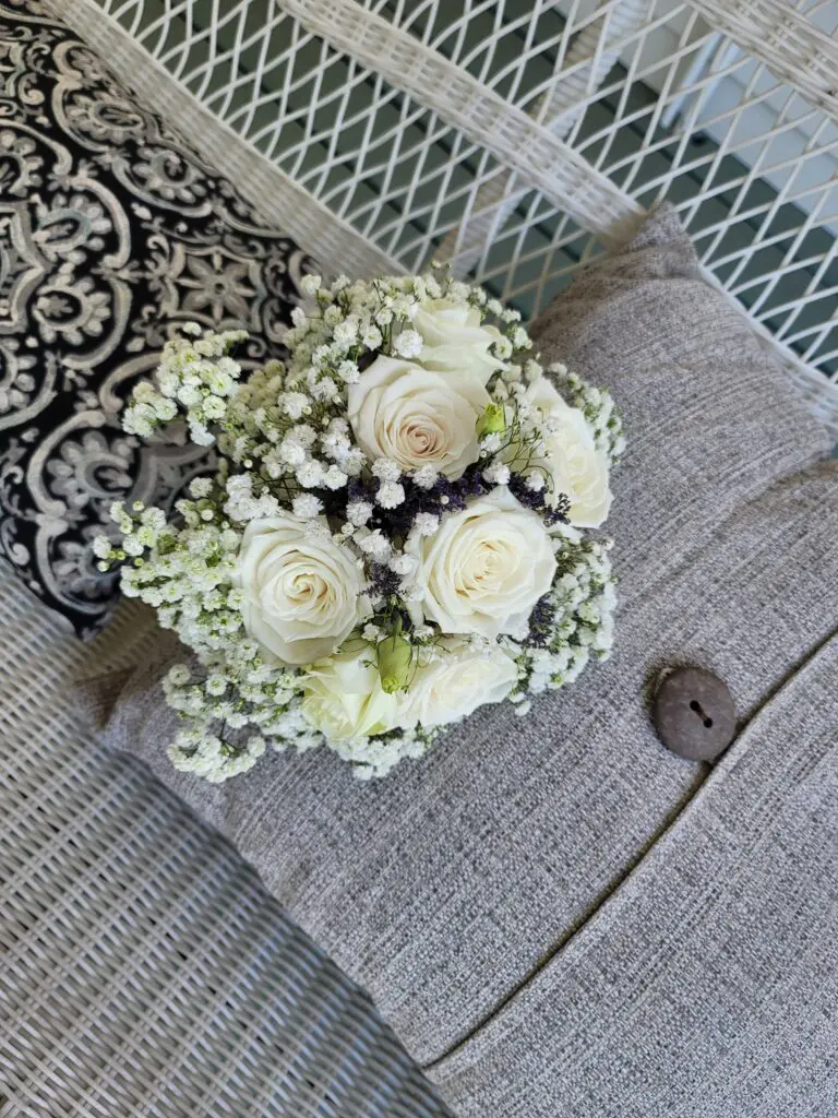 A bouquet of white roses and baby 's breath is sitting on a couch.