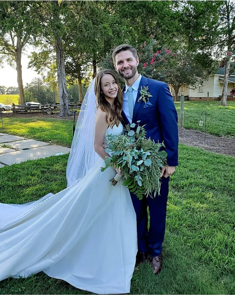 A bride and groom are posing for a picture in the grass.