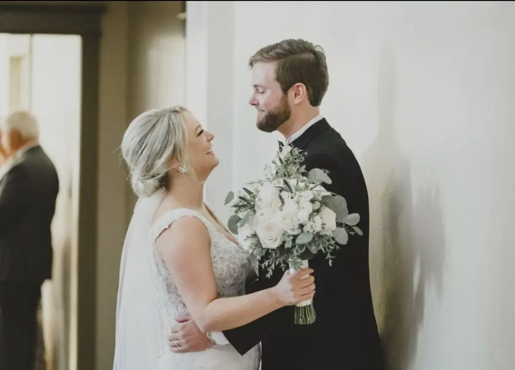 A bride and groom are standing next to each other holding a bouquet of flowers.